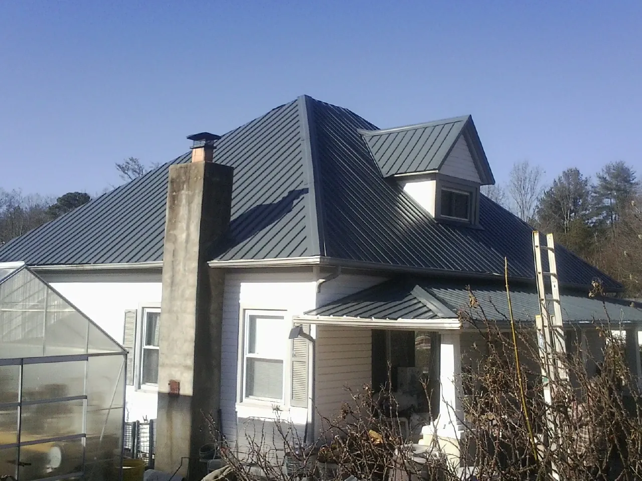 Dark blue standing seam metal roof on a white farmhouse with dormer — Slate & Tile Roof Repair by Roofing Brothers in Mc Calla