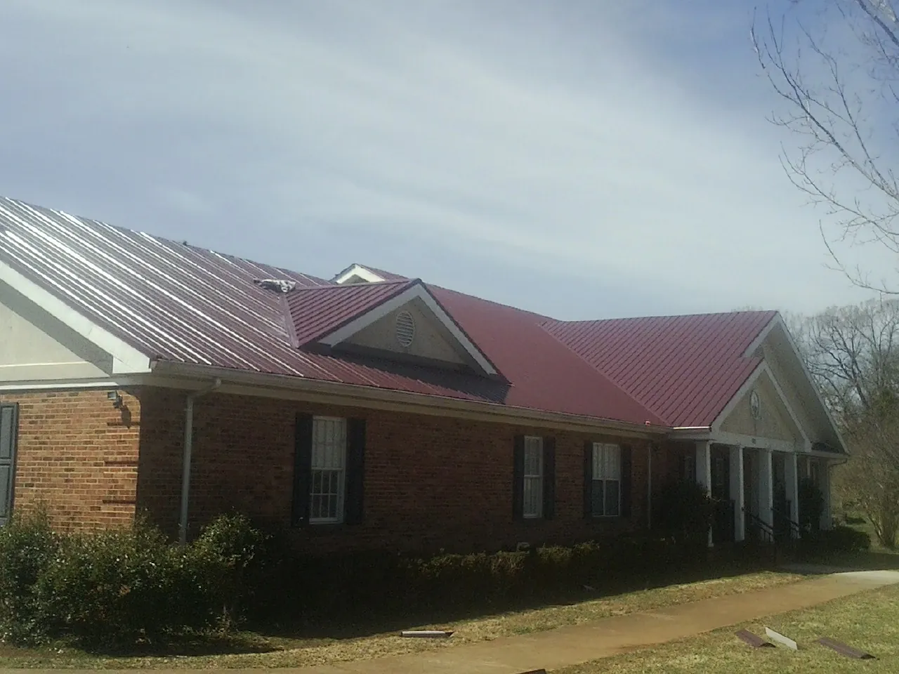 Red metal roof with gabled entries on a long brick building, from a Hail Damage Roof Repair job in Mc Calla