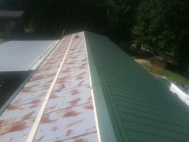 Old rusted panels beside newly installed green metal roofing — Wind Damage Roof Repair by Roofing Brothers in Mc Calla