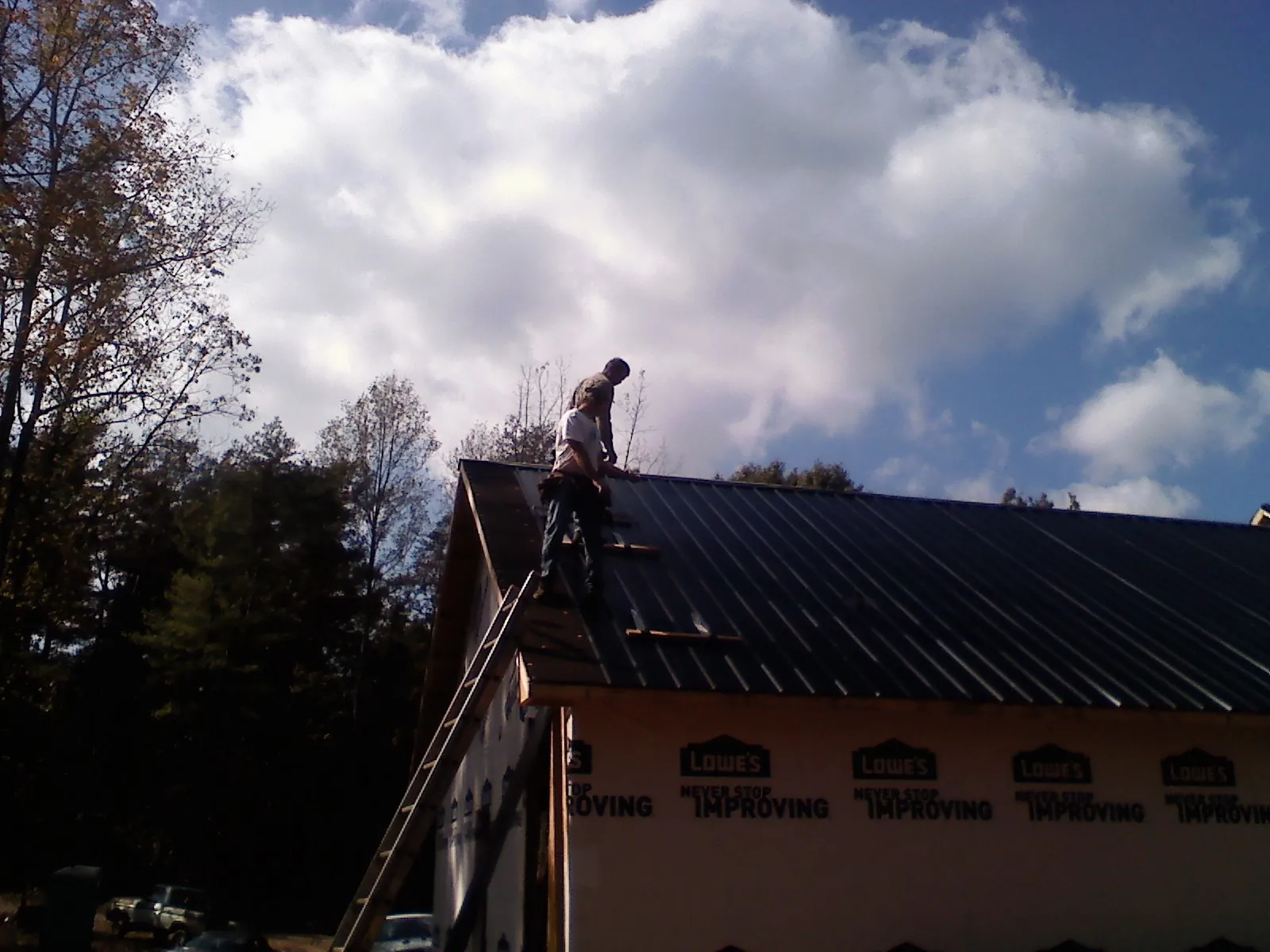 Roofer fastening dark metal panels high against a cloudy sky, from a Roof Inspection job in Mc Calla