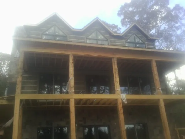 Dormers and porch framing on a large log home under construction — Roof Coating work by our crew in Mc Calla