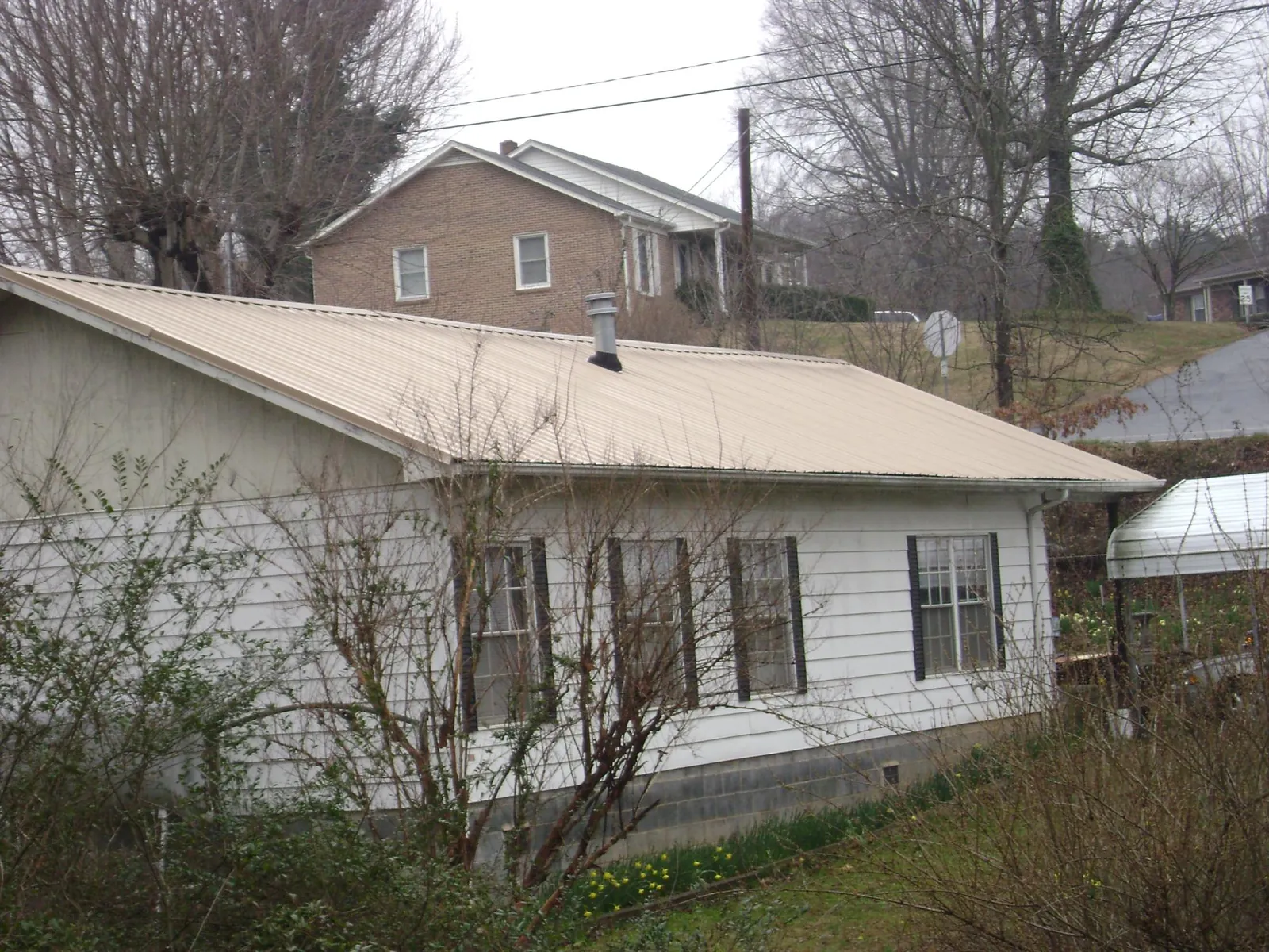 Tan metal roof on a white sided house set into a hillside — Commercial Roofing by Roofing Brothers in Mc Calla